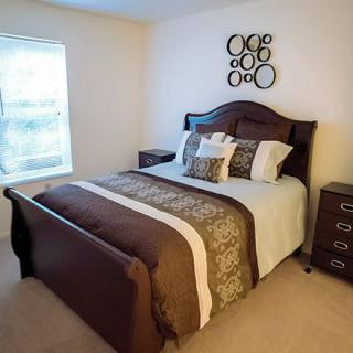 A neatly arranged bedroom with a bed featuring decorative pillows and dark wood furniture.