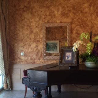 An elegant interior featuring a piano adorned with flowers and framed photos, set against a textured wall with a mirror.