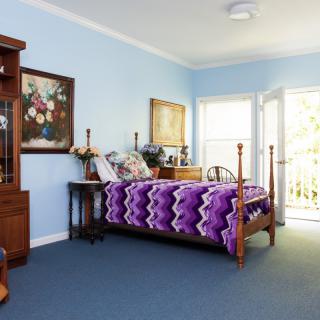 A cozy bedroom with a wooden bed and purple blanket, light blue walls, and decorative paintings.