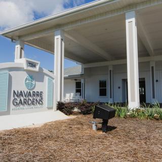 A modern building with columns and a sign reading 'Navarre Gardens Assisted Living Facility'.