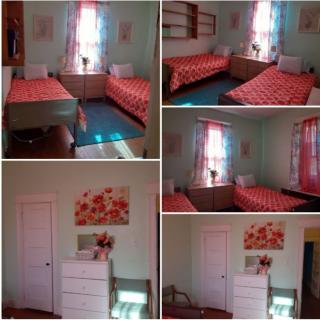 A cozy bedroom featuring twin beds with floral bedspreads, bright curtains, and a chest of drawers.
