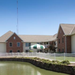 A brick building with a fenced pond and an umbrella on the patio under a clear blue sky.