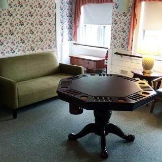 A cozy living room with a vintage poker table, green sofa, and a lamp near the window.