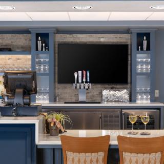 A modern bar setup with a sleek counter, drinks on display, and a television mounted above.