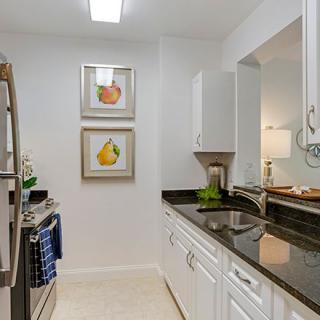 A modern kitchen with white cabinets and stainless steel appliances, featuring colorful artwork on the wall.