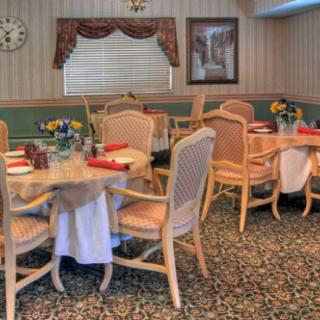 A cozy dining area with elegantly set tables, cushioned chairs, and floral decorations.