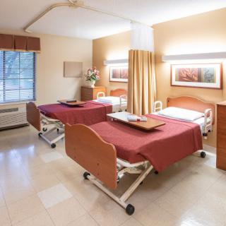 A hospital room with two beds separated by a curtain, featuring medical equipment and a large window.