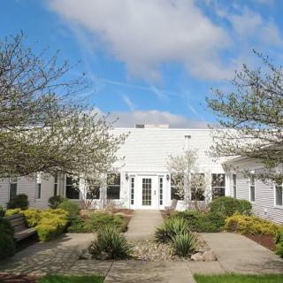 A white building with a courtyard featuring greenery and trees under a blue sky.
