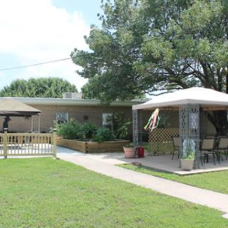A charming house with a patio and garden, surrounded by green grass and trees.