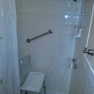 A bathroom shower with a grab bar and shower chair.