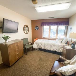 A cozy bedroom with a single bed, wall-mounted television, and a view outside the window.