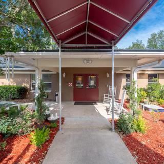 An entrance to a building with a red canopy, surrounded by landscaped gardens.