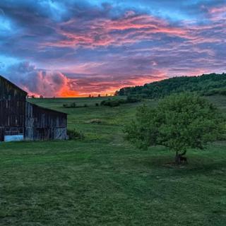 A serene sunset over a peaceful farm, with vibrant clouds illuminating the sky.