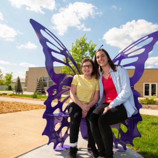 Two friends enjoying a sunny day together on a butterfly-themed bench in the park.