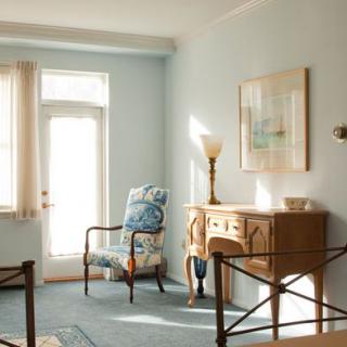 A cozy living room with vintage furniture, featuring a patterned armchair and a wooden desk under soft daylight.