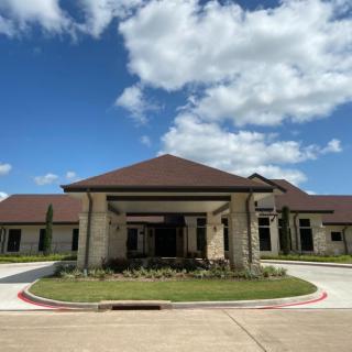 A modern, single-story building with a prominent entrance, surrounded by a clear blue sky and scattered clouds.