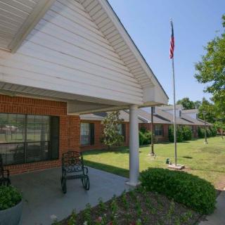 A porch with rocking chairs and a flagpole outside a brick house on a sunny day.