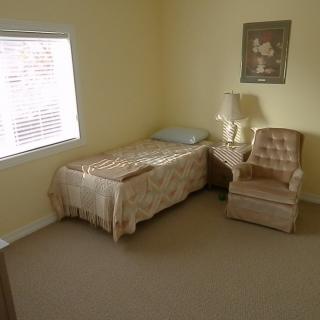 A minimalist bedroom with a single bed, chair, and lamp by the window.