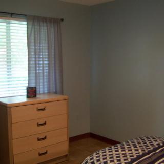 A simple bedroom with a dresser and a window with curtains.