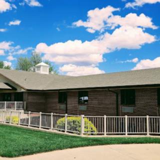 A modern single-story house with a white fence under a bright blue sky with clouds.