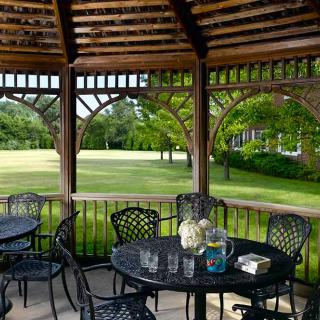 A peaceful outdoor gazebo with tables and chairs overlooking a lush green lawn.