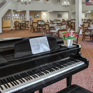 A grand piano with sheet music and flowers on top, located in a spacious dining area.