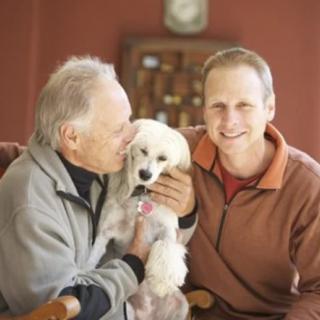 Two men happily pose with their dog indoors.