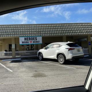 A storefront in a strip mall with a white car parked outside.