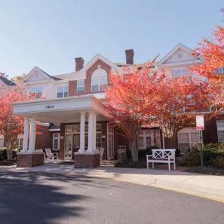 A brick building with a portico entrance, surrounded by trees with vibrant red autumn leaves.