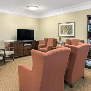 A cozy living room with armchairs facing a television, featuring warm colors and a carpeted floor.