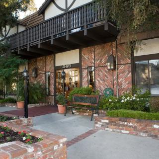A brick building exterior with a balcony, surrounded by plants and a bench.