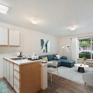 A modern apartment living area with an open kitchen, cozy sofa, and large windows allowing natural light.