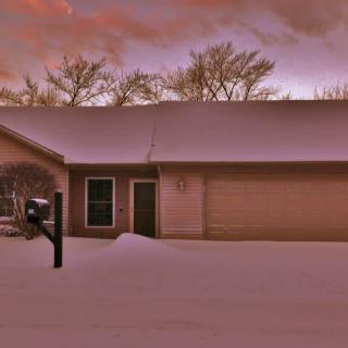 A snow-covered house at sunset with a peaceful winter landscape.