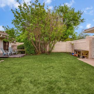 A tranquil backyard with a lush green lawn and surrounding trees, complemented by patio seating for outdoor relaxation.