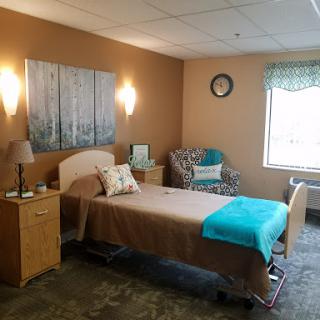 A well-lit hospital room featuring a bed, chair, and warm decor.