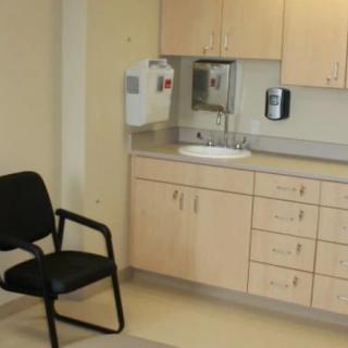 A small clinic room with a chair, cabinets, and a sink.