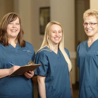 Three healthcare professionals in blue scrubs smiling together.
