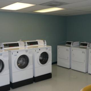 A laundry room with multiple washing machines and dryers lined up against the wall.