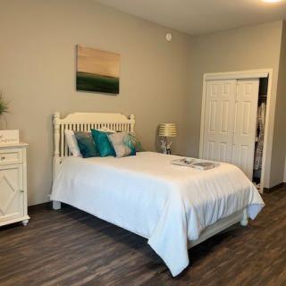 A cozy bedroom featuring a white bed with colorful cushions, wooden flooring, and a neatly decorated interior.