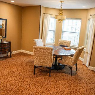 A cozy dining room with a round table and upholstered chairs, featuring a warm color palette and natural lighting from large windows.