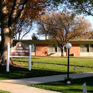 A peaceful view of a building surrounded by trees and well-maintained grass.
