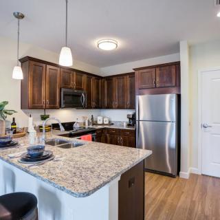 A modern kitchen featuring wooden cabinets, stainless steel appliances, and a granite countertop with bar seating.