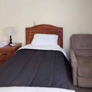 A simple bedroom setup with a single bed, nightstand, lamp, and a comfortable chair.