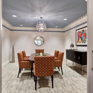 A stylish dining room with a chandelier, colorful artwork, and upholstered chairs.