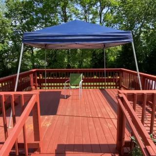 A sunny outdoor deck with a blue canopy and a single chair.