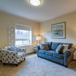 A cozy living room featuring a blue sofa, patterned armchair, and a soft carpet.