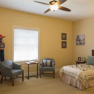 A cozy bedroom with a bed, two chairs, and a side table under a ceiling fan.