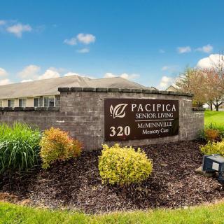 A view of a sign for Pacifica Senior Living with landscaping and a building in the background.
