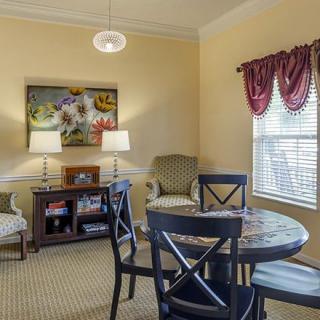 A cozy living room with a table and chairs, decorated with lamps, artwork, and curtains.