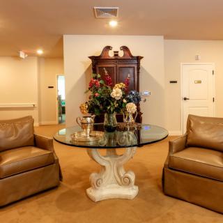 A cozy living room with two brown armchairs and a glass-top table adorned with flowers.